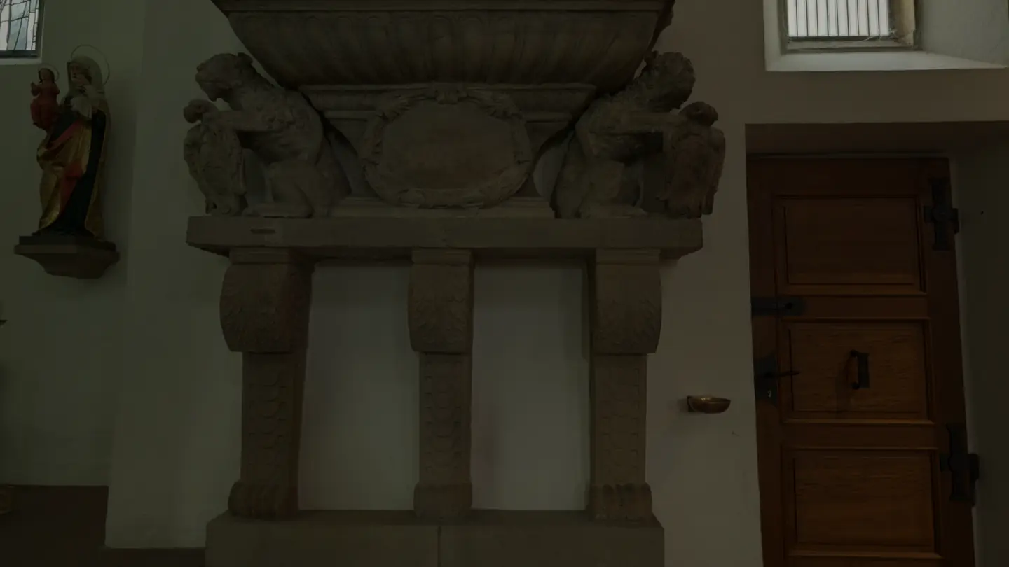 A side aisle of St. Moriz: a carved stone epitaph, a wooden door and a gilded side altar