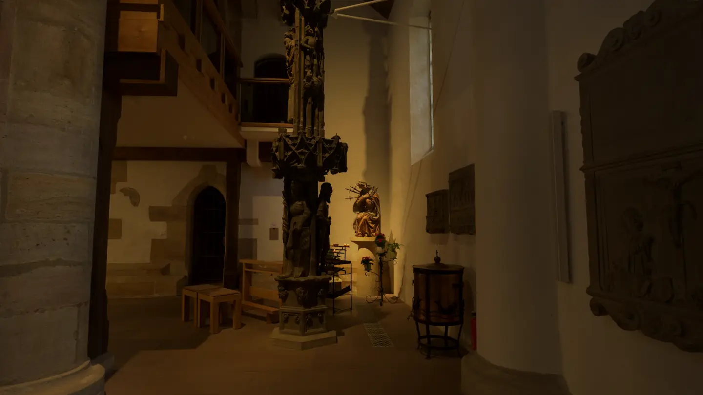 A statue of Our Lady of Sorrows among votive candles, beside the carved Gothic column of the old market fountain, in St. Moriz